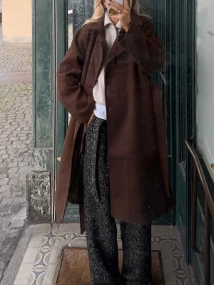 Brun oversized kappa (NA-KD) - Snygg brun oversized kappa i ullmix med bred krage och knäppning framtill. Kappan har en avslappnad passform och bälte i midjan för en cool look. Perfekt för lager-på-lager och trendiga outfits under höst och vinter. Nakd 