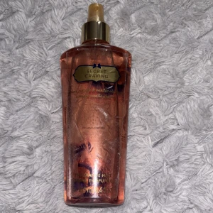 Victoria's Secret Secret Craving mist - En parfymmist från Victoria's Secret i doften Secret Craving. Flaskan är rosa med guldfärgad spraykork och har en elegant, rektangulär form. Doften har inslag av svartvinbär och vanilj, vilket ger en söt och fruktig känsla.