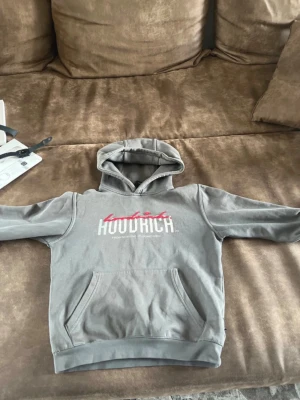 Grå HOODRICH hoodie med tryck - Säljer en grå hoodie från HOODRICH som jag köpte från jd sports den är lite sliten men är väldigt skön och fin. Storleken är M 10-12 år