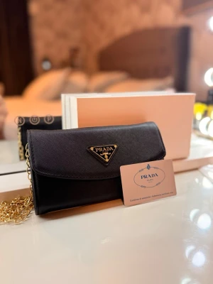 Svart handväska från Prada med kedja - Svart handväska från Prada i elegant läder med guldfärgad kedjerem. Väskan har det klassiska triangulära Prada-emblemet framtill och stängs med lock. ( ÄKTA kommer med certifikat kort!!! ) 