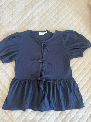 Mörkblå topp med knyt från Gina Tricot - Supersöt mörkblå topp från Gina Tricot med puffärmar och tre dekorativa knyt framtill. Toppen har en lätt utställd nederdel och rund halsringning. Perfekt för dig som vill klä upp dig till vardags☀️💕
