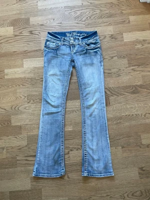 Ljusblå bootcut jeans från WallFlower - Säljer ett par ljusblå bootcut jeans från WallFlower med slitna detaljer och broderade bakfickor. Jeansen har låg midja och klassisk femficksdesign. Perfekta för dig som gillar en avslappnad och trendig stil. Storlek 3 vilket ungefär motsvarar w26 och xs/s💕