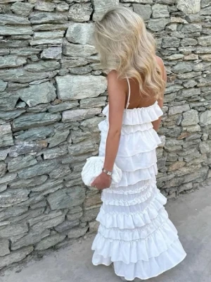 Vit långklänning med volanger - Säljer en vit långklänning med tunna axelband och flera lager volanger. Klänningen har öppen rygg och  siluett som passar perfekt till sommaren. Klänningen är i storlek xs, men passar s och kanske m pga att den är stretchig i materialet. Från H&M säljs inte längre🤗