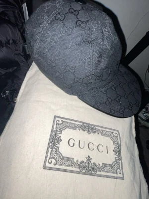 Svart keps med GG mönster  - Säljer en svart keps med GG mönster över hela kepsen, svart skön keps om du vill ha en lyxigare stil den har ett kardborreband där du kan ändra storlek på.