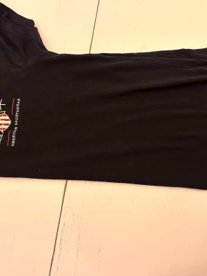 Svart t-shirt från Gant - Snygg svart t-shirt från Gant med broderad logga och texten 'American Sportswear' på bröstet. T-shirten har korta ärmar och är tillverkad i mjuk bomull. Perfekt för en avslappnad och stilren look.