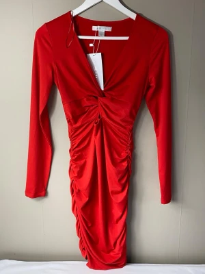 Röd omlottklänning från newyorker - Oanvänd med prislapp kvar. Snygg röd omlottklänning från newyorker med v-ringning och långa ärmar. Klänningen har draperade detaljer framtill och baktill. Tillverkad i ett mjukt, stretchigt material som sitter bekvämt.