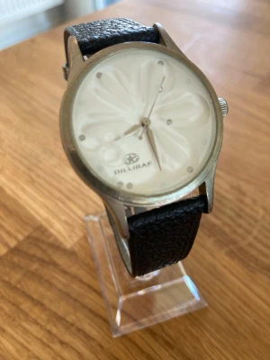 Dilligaf ”The Flower” 36mm Damur - Dilligaf D200120 klocka med ett svart armband i äkta läder och ett boett i rostfritt stål. Urtavlan är vit med ett ovanligt blommönster. Klockan är batteridriven och behöver nytt (kvarts). Skick enligt bilder.  Nypris: 500 SEK Mitt pris: 189 SEK  Skickas alltid snabbt och spårbart. Skriv vid frågor och se gärna mina andra annonser!   GRATIS: För betalande kunder erbjuder jag personlig experthjälp för dig att göra nya fynd (nytt & begagnat). Fråga för mer info!
