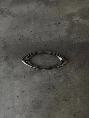 Oakley kabinhakr - Säljer en ovalformad accessoar i blank silverfärg, tillverkad i metall. Perfekt som detalj till väskor, bälten eller som dekoration på kläder. Enkel och stilren design från Oakley