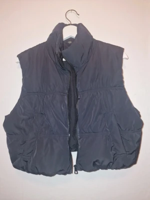 Svart väst - Snygg väst med dragkedja framtill. Västen har två fickor på sidorna och en puffig, quiltad look. Perfekt att slänga över en hoodie för en chill och trendig stil.