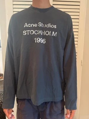 Acne studios longsleeve - Cool svart långärmad topp från Acne Studios med tryck 'Acne Studios STOCKHOLM 1996' i vitt framtill. Oversized passform och rund halsringning. Perfekt för en avslappnad och trendig look.