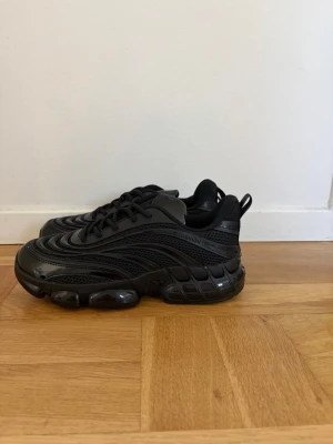 Svarta chunky sneakers med meshdetaljer - Säljer ett par svarta chunky sneakers med futuristisk design och meshdetaljer. Skorna har en kraftig sula med bubblor och vågformade linjer på ovandelen. Perfekta för dig som gillar streetwear och vill sticka ut med din stil.