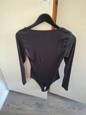 Svart ribbad långärmad body - Säljer en svart ribbad body med långa ärmar och rund hals. Bodyn har en enkel och stilren design, perfekt att matcha med olika outfits. Materialet är stretchigt och följsamt för en bekväm passform.