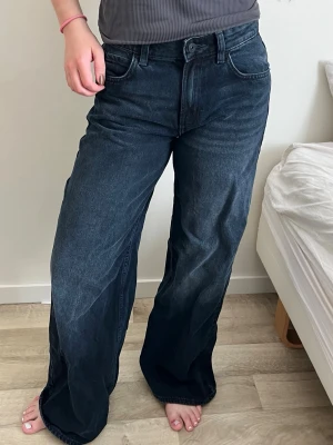 Mörkblå baggy jeans med hög midja - Säljer ett par mörkblå baggy jeans med mellan midja och vida ben. Jeansen har klassisk femficksmodell och knappgylf. Perfekta för en avslappnad och trendig look. Materialet är kraftig denim i bomull.