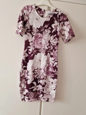 Blommig kortklänning från B.Young - Supersnygg kortklänning från B.Young med stora blommor i vitt och vinrött. Klänningen har rund halsringning och korta ärmar. Materialet känns mjukt och stretchigt, perfekt för dig som gillar en feminin och bekväm stil.