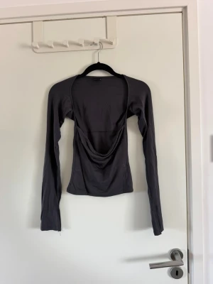 Mörkgrå långärmad topp - Säljer en mörkgrå långärmad topp med djup urringning. Toppen har en slim passform och är tillverkad i mjukt, stretchigt material som känns skönt mot huden. Perfekt för dig som gillar minimalistisk och stilren design. Använd