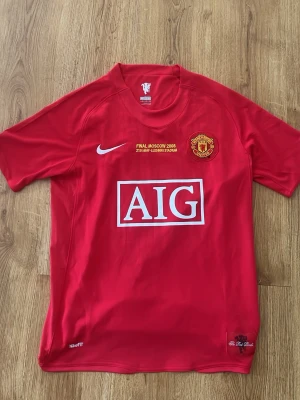 Manchester United Ronaldo tröja - Säljer en röd Manchester United matchtröja från Nike med AIG som sponsor, klubbmärke på bröstet och trycket 'Final Moscow 2008'. På ryggen står det Ronaldo och nummer 7. Tillverkad i lätt och ventilerande material, perfekt för fotboll eller samling.