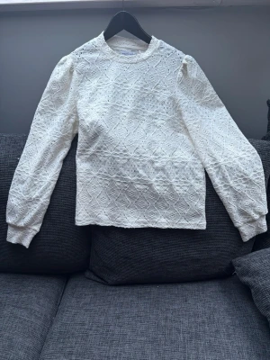 Vit spetsblus/tröja från Holly & Whyte - Säljer en vit spetsblus/långärmad tröja från Holly & Whyte by Lindex. Tröjan har ett vackert spetsmönster, rund halsringning och långa ärmar med lätt puff vid axlarna. Perfekt för dig som gillar romantisk och stilren look.