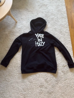 Svart hoodie från Dondup - Snygg svart hoodie från Dondup med trycket 'MADE IN ITALY' i vitt och grått på bröstet. Klassisk huva och känguruficka framtill. Tillverkad i mjukt bomullsmaterial som känns skönt mot huden. Perfekt för en avslappnad och trendig look. Sällan använd då de var ett impulsivt köp och de är små i storlek. Pris kan diskuteras