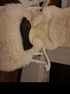 Svarta tofflor med broderi - Säljer ett par svarta tofflor med snyggt brunt och beige broderi på ovansidan. Tofflorna har en klassisk slip-in modell och är gjorda i ett mjukt material som ser bekvämt ut. Perfekta för att chilla hemma.