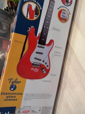 Elektronisk leksaksgitarr MeMe Music - Elektronisk leksaksgitarr i röd och vit plast med metallsträngar, ljuseffekter och 8 demolåtar. Gitarren har realistiskt ljud och medföljande axelband. Perfekt för unga musikälskare som vill rocka loss hemma.