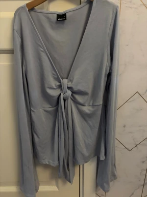 Ljusblå långärmad topp med knyt - Trendig ljusblå långärmad topp från GINA TRICOT med djup v-ringning och knytning framtill.  Den har en slim passform som framhäver siluetten. Perfekt för att skapa en stilren och modern look.
