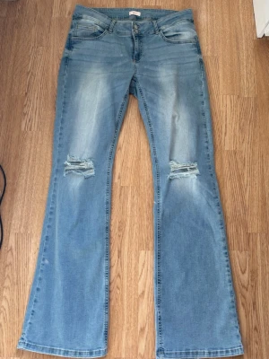 Low waist slitna Nelly jeans - Nästan helt oanvända. Ljus blå jeans från Nelly men slitna knän och fickor med knapp.