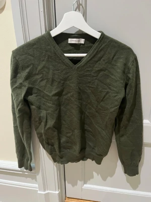 Olivgrön V-ringad tröja Chevalier - Snygg olivgrön tröja från Chevalier med V-ringning och långa ärmar. Tillverkad i mjuk ull  som passar perfekt till lager-på-lager tex vid jakt. Klassisk och enkel design med ribbade muddar vid ärmslut och nederkant.
