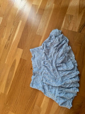 Blå volangkjol från 157, storlek S - Söt ljusblå kortkjol från 157 med små vita blommor och volangdetaljer. Kjolen har resår i midjan för skön passform och är perfekt för vår och sommar. Materialet känns lätt och luftigt, vilket gör den enkel att bära till olika outfits.