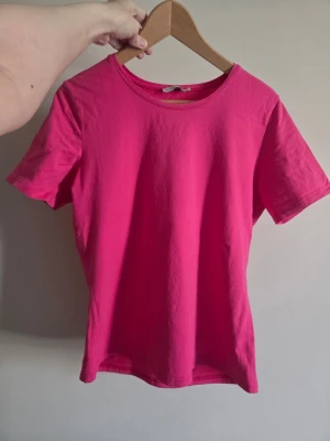 Snygg och enkel t-shirt i stark rosa färg💕 - En mjuk och bekväm bas-tröja i härlig rosa nyans som är perfekt till både vardag och mer avslappnade outfits Sitter snyggt på kroppen och är lätt att styla med jeans, kjol eller shorts💕  Perfekt som sommarplagg eller som lager-på-lager under jacka/cardigan☀️  ⚠️OBS: Svårt att fånga exakt färg på bild. Finns även ett litet hål som knappt syns (se bild 4).  🎀Färg: Rosa 🎀Storlek: Märkt L men uppskattas som S/M beroende på önskad passform 🎀Skick: Fint skick, lite små nopprig  💌Skriv vid frågor 