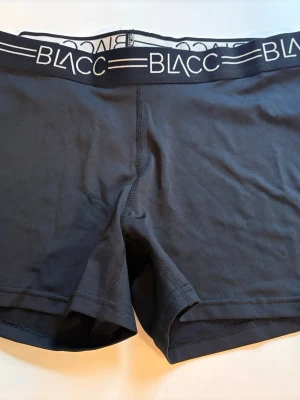 Svarta träningsshorts från BLACC - Snygga svarta träningsshorts från BLACC med bred resår i midjan där loggan syns tydligt. Tillverkade i mjukt och stretchigt material som sitter skönt på kroppen. Perfekta för träning eller vardag när du vill ha komfort och stil.