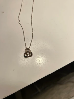 Pärlhalsband med hjärthänge - Säljer ett stilrent halsband med vita pärlor och ett silverfärgat hjärthänge. Perfekt accessoar för att lyfta din outfit med en söt och klassisk touch. Kedjan är gjord av små, runda pärlor och hänget är i metall med spegelblank finish.
