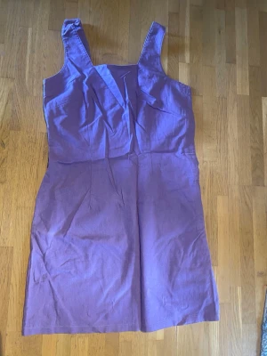 Linneklänning - Snygg lila klänning i linne/bomull med breda axelband och knappar längs ena sidan. Klänningen har en rak passform och stilrena sömdetaljer framtill. Perfekt för dig som gillar en enkel men trendig look.