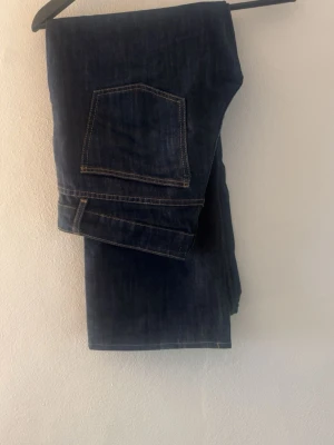 Mörkblå raka jeans - Säljer ett par mörkblå raka  jeans med klassiska fickor och kontrastsömmar. Jeansen har låg midja och är tillverkade i ett mjukt denimtyg som sitter snyggt på kroppen. Perfekta för dig som gillar en avslappnad men ändå trendig look. Uppsydda till att dem passar någon som är ca 163