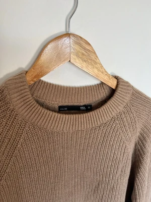 Beige stickad tröja från 157 - Säljer en beige stickad tröja från 157 med rund halsringning och grovstickad struktur. Tröjan har långa ärmar och ribbade muddar vid hals, ärmslut och nederkant. Perfekt för lager på lager under kyliga dagar. Strlek M. Mycket fint skick