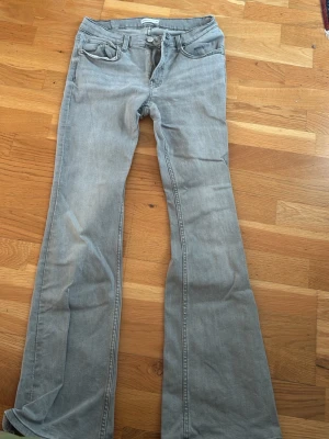 Ljusgrå bootcut jeans - Säljer ett par ljusgrå bootcut jeans med klassisk femficksdesign och normal midja. Jeansen har utsvängda ben och är tillverkade i mjukt denimtyg. Perfekta för dig som gillar en avslappnad men trendig look.