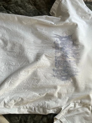 Vit t-shirt med abstrakt tryck - Vit t-shirt med korta ärmar och ett abstrakt, blågrått tryck på framsidan. Klassisk passform och rund halsringning. Perfekt för en avslappnad och stilren look.