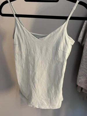 Ljusgrå enkel linnetopp - Säljer en ljusgrå linnetopp med smala axelband och v-ringad hals. Toppen är ärmlös och har en clean, minimalistisk look som passar perfekt till sommaren. Tillverkad i mjuk bomull för en bekväm känsla.