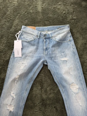 Dondup George  - Säljer ett par ljusblå jeans från Dondup med trendiga slitningar och skinny fit. Jeansen har klassisk femficksmodell, låg midja och är tillverkade i stretchigt denim för skön passform. Perfekta för en avslappnad och cool stil.