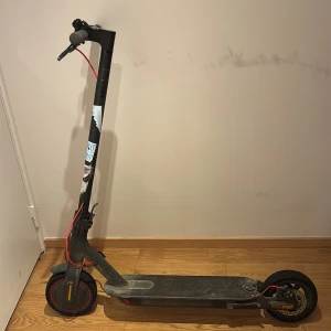 Svart elscooter med röda detaljer - Elektrisk sparkcykel som går i 25/h. Modellen är Xiaomi mi 2 PRO som original priset ligger på 5000 kr. Den är enkel att ta med som tex buss eller tåg i och med att du kan vika den. Men dena så får du även en laddare. Den har punkfria däck som är perfekt så du inte behöver få punka hela tiden 