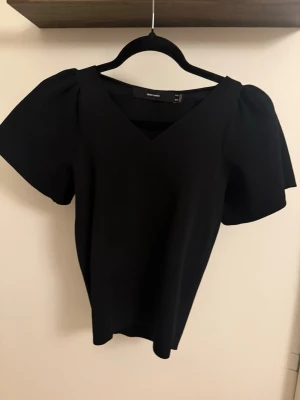 Svart v-ringad topp från Vero Moda - Stilren svart topp från Vero Moda med v-ringning och korta, puffiga ärmar. Toppen har en enkel och elegant design som passar perfekt till många olika looks. Tillverkad i ett mjukt material som känns skönt mot huden.