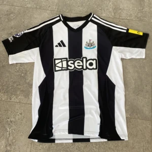 Newcastletröja - Snygg Newcastle United matchtröja från Adidas i klassiskt svartvitt randigt mönster. Helt NY med Isak 14 på ryggen i storlek L