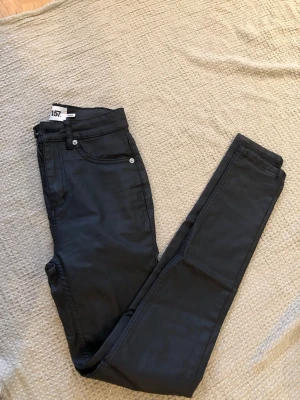 Svarta coated jeans från Lager 157 - Snygga svarta coated jeans från Lager 157 i modellen Snake. Jeansen har en tight passform och är gjorda i ett stretchigt material med 77% rayon, 20% nylon och 3% elastan. Perfekta för dig som gillar en stilren och trendig look.