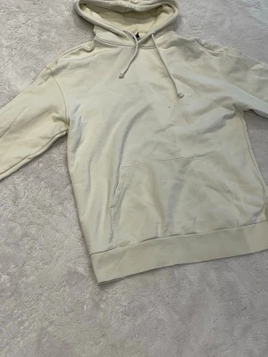 Beige hoodie med ficka framtill - En stilren beige hoodie med huva och dragsnören. Hoodien har en stor känguruficka framtill och ribbade muddar vid ärmslut och nederkant. Perfekt för en avslappnad och trendig look. Materialet känns mjukt och bekvämt, troligen bomull eller bomullsblandning.