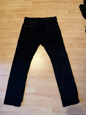 Svarta Levi's raka jeans - Säljer ett par svarta jeans från Levi's med klassisk rak passform. Jeansen har fem fickor, bälteshällor och Levi's ikoniska läderpatch bak i midjan. Perfekta för en clean och tidlös look. Materialet är kraftig denim i bomull.