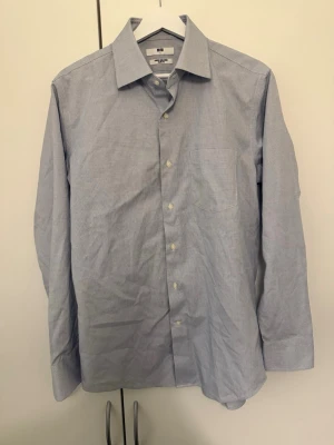 Ljusblå slim fit skjorta från Uniqlo - Snygg ljusblå skjorta från Uniqlo i slim fit-modell. Skjortan är super non-iron och har ett diskret rutmönster, klassisk krage, bröstficka och långa ärmar. Perfekt för en clean och stilren look.