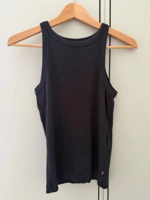 Svart ribbad linnetopp från Levi's - Säljer en svart ribbad linnetopp från Levi's. Toppen är ärmlös med breda axelband och har en klassisk, enkel design. Perfekt att matcha med jeans eller kjol för en clean look.