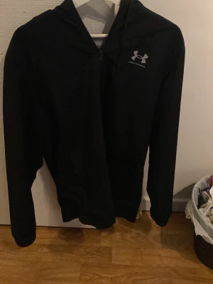 Vindjacka från Under Armour - Snygg vindjacka hoodie från Under Armour med dragkedja framtill och logga på bröstet. Tillverkad i ett mjukt och lätt material som passar perfekt till träning eller chill. Klassisk passform med långa ärmar och huva.