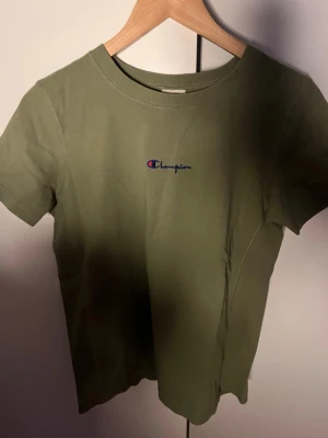 Olivgrön Champion t-shirt -  Olivgrön t-shirt från Champion med klassisk logga broderad på bröstet. Köpt många år sedan så kommer inte till någon användning. Köpt på Urban outfiters, perfekt present till lillebrorsan osv. Unisex storlek