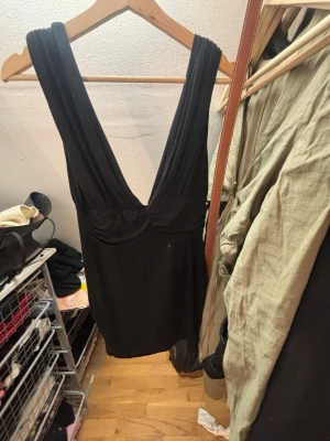 Svart kort klänning djup v-ringning - Snygg svart kort klänning med djup v-ringning både fram och bak. Klänningen har breda axelband och en figurnära passform som framhäver siluetten. Perfekt för dig som vill ha en stilren och enkel look med en touch av edge. Köpt på sellpy men aldrig använd, från asos