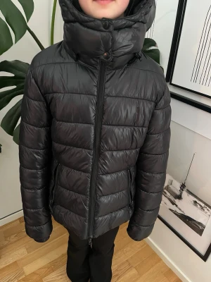 Svart pufferjacka med luva - Svart glans jacka från lager 157. Det finns ett litet hål ish 2 cm, syns knappt. 